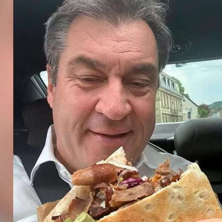 Close-up of Markus Söder in a car, smiling down at a large Döner Kebab he is holding.